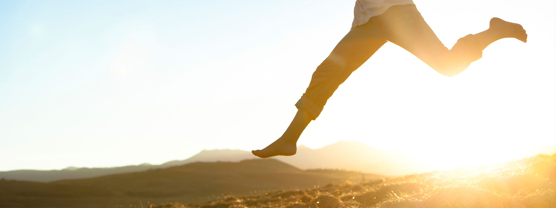 Feminine person jumping in an open field at sunset.